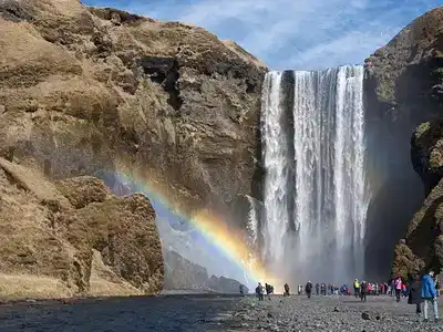 Group of tourists viewing a waterfall with a rainbow in front of them.