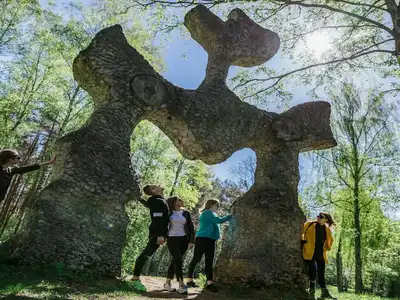 Three people standing beneath the arch of an old stone monument in the Europas Parkas open air museum